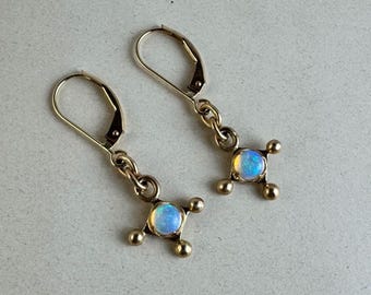 May include: A pair of gold-tone leverback earrings, each featuring a central round cabochon opal with iridescent blue and white flashes, set within a four-pronged square frame with small spherical accents at each corner of the setting.