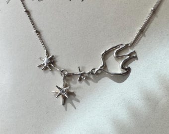 May include: A delicate silver necklace featuring a celestial design. The necklace includes star-shaped pendants and a stylized abstract shape. The chain is fine and detailed, with small bead accents. The design is elegant and suitable for everyday wear.