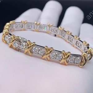 May include: A gold and silver bracelet with multiple clear gemstones. The bracelet features gold X-shaped accents and is set with multiple clear gemstones. The bracelet is a piece of jewelry.