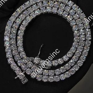 May include: A dazzling diamond tennis necklace. The necklace features multiple rows of round-cut, sparkling diamonds, set closely together. The diamonds are clear and reflect light, creating a brilliant display. The necklace is displayed on a black surface.