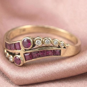 May include: A gold ring with a double band design. The top band features a row of small, round diamonds. The lower band is adorned with square-cut rubies. The ring also has larger, round rubies.