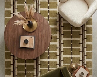 Puede incluir: Una vista cenital de una alfombra rectangular con un patrón geométrico de cuadrícula en verde oliva y crema. La alfombra está dispuesta con una mesa de centro redonda de madera, un sillón texturizado color crema, un sillón verde oscuro y una mesa auxiliar.