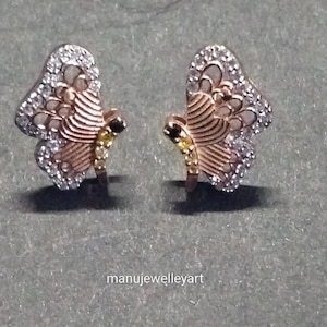 May include: A pair of butterfly earrings. The earrings have a gold-coloured body with white and yellow gemstones. The wings are outlined with white gemstones, and the body has a striped design. The earrings are set against a grey background.