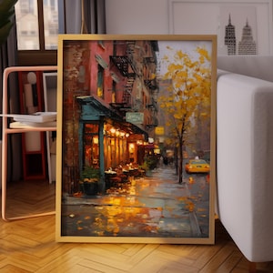 Puede incluir: Pintura enmarcada que representa una escena de calle lluviosa con un café, un taxi amarillo y árboles de otoño. La obra utiliza tonos cálidos y dorados de las luces del café y los reflejos en el pavimento mojado. El marco es de color madera clara.