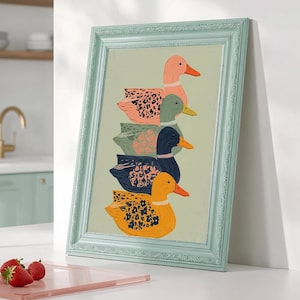 Może przedstawiać: Oprawiony wydruk przedstawiający stos pięciu kolorowych kaczek. Kaczki są w odcieniach różu, zieleni, niebieskiego i żółtego, każda z unikalnymi wzorami. Rama jest w kolorze jasnoniebieskim, a grafika jest wyświetlana na białej powierzchni.