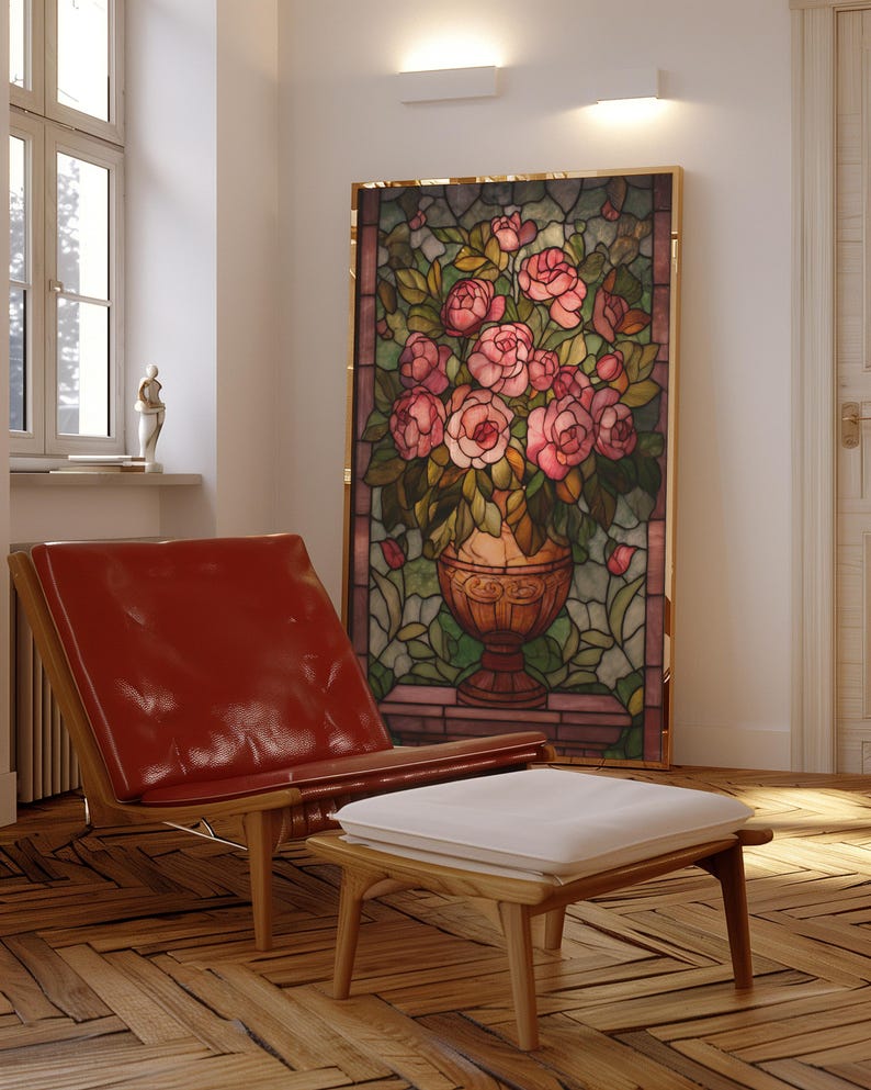 May include: A stained glass panel featuring a vase overflowing with pink roses, set in a gold frame. A red leather chair and a wooden ottoman with a white cushion are in the foreground. The room has a hardwood floor and natural light.
