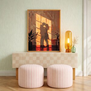May include: A framed artwork depicts a couple embracing in front of a window, bathed in warm light. The scene is set in a room with a checkered cabinet, two pink striped ottomans, and a glowing amber lamp. A potted plant and small table with flowers complete the decor.