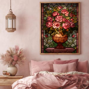 May include: A framed stained glass artwork depicts a vase overflowing with pink roses and green leaves. The vase is a warm, golden color, set against a backdrop of green and brown glass. The artwork is displayed above a bed with pink bedding.