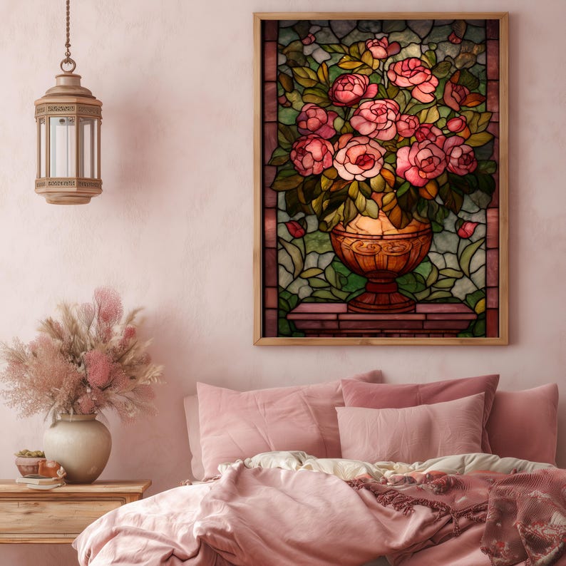 May include: A framed stained glass artwork depicts a vase overflowing with pink roses and green leaves. The vase is a warm, golden color, set against a backdrop of green and brown glass. The artwork is displayed above a bed with pink bedding.
