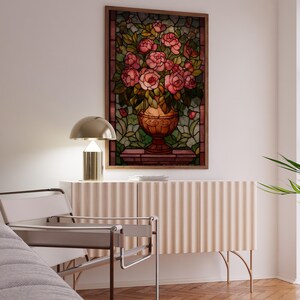 May include: A framed stained glass artwork featuring a vase overflowing with pink roses. The artwork hangs above a light-colored cabinet with a ribbed design. A modern chair and a gold lamp are also visible.