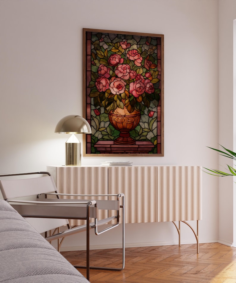 May include: A framed stained glass artwork featuring a vase overflowing with pink roses. The artwork hangs above a light-colored cabinet with a ribbed design. A modern chair and a gold lamp are also visible.