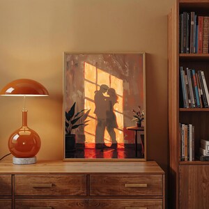 May include: A framed artwork depicts a couple embracing in front of a sunlit window. The painting uses warm tones of orange, brown, and red. A matching orange lamp with a marble base sits on a wooden dresser. A bookshelf is visible on the right.