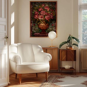 May include: A cozy living room scene featuring a white armchair, a stained glass artwork of roses in a vase, and a decorative lamp. A wooden side table holds a potted plant and a small decorative bowl. A patterned rug adds warmth.
