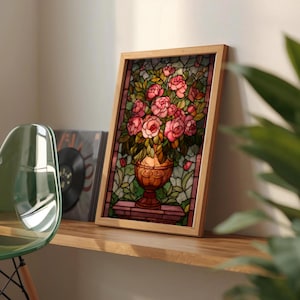 May include: A framed stained glass artwork featuring a bouquet of pink roses in a decorative vase. The artwork is set against a backdrop of green foliage and is framed in light wood. The artwork is displayed on a wooden shelf.