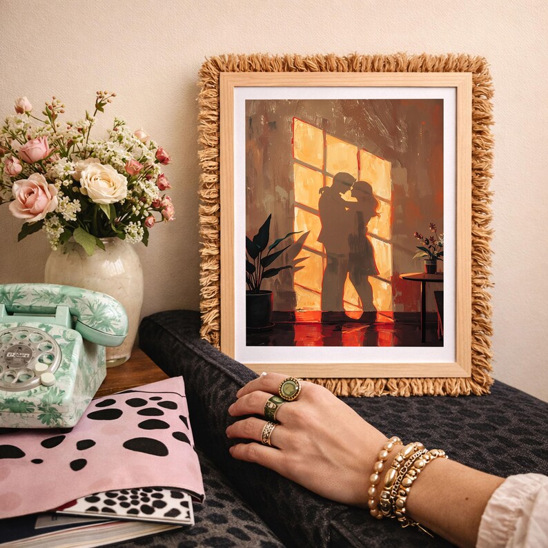 May include: A framed art print depicts a couple embracing in front of a sunlit window. The artwork is in a wooden frame with a fringed border. A vase of flowers, a vintage telephone, and a pink pouch with a black and white pattern are also visible.