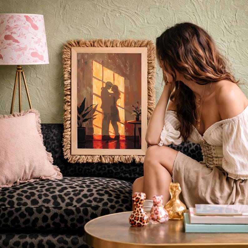 May include: A framed artwork depicts a couple embracing in a warm, sunlit room. The painting is in a wooden frame with a fringed border. A pink lampshade and a leopard-print sofa are in the background. Decorative vases sit on a table.