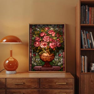 May include: A framed stained glass artwork featuring a bouquet of pink roses in a decorative vase. The artwork has a gold frame and is set against a backdrop of green leaves and a brown border. The vase is a warm brown color.