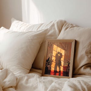 May include: A framed artwork depicts a couple embracing in a warm, sunlit room. The painting features a palette of oranges, reds, and browns, with a silhouette of the figures. The artwork is displayed on a bed with white linens.