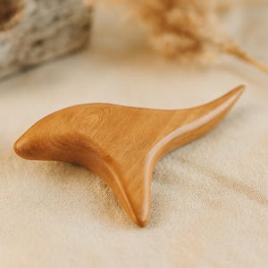 May include: A wooden gua sha tool with a smooth, curved design. The tool is made of light brown wood and has a polished finish. The gua sha tool is designed for facial massage and relaxation.