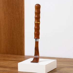 Peut inclure: Un gratte-dos en bois avec un manche en forme de bambou et une extrémité incurvée pour gratter. La poignée est de couleur marron foncé avec un accent doré. L'extrémité grattante comporte une série de petites dents. Le gratte-dos est présenté sur un bloc blanc.