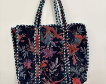 May include: A navy blue tote bag with a floral pattern featuring birds and foliage in shades of red, purple, and green. The bag has striped handles and trim, and is designed for carrying items.