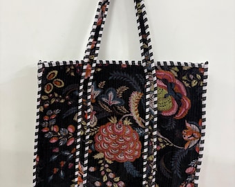 May include: A black tote bag with a floral pattern in shades of red, pink, and green. The bag has a corduroy texture and is trimmed with a black and white striped border. The handles are also black and white striped.