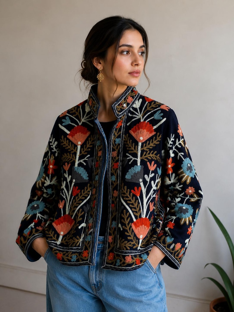 Pu&ograve; includere: Una giacca blu navy scuro con colletto alto e maniche lunghe, decorata con intricati ricami floreali nei toni dell'arancione, azzurro e bianco. La giacca ha una linea dritta ed &egrave; indossata sopra un top nero e un paio di jeans blu.