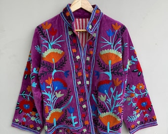 May include: A purple velvet jacket with vibrant floral embroidery in orange, blue, and teal. The jacket features a high collar and is hanging on a wooden hanger against a neutral background. The embroidery design is symmetrical.