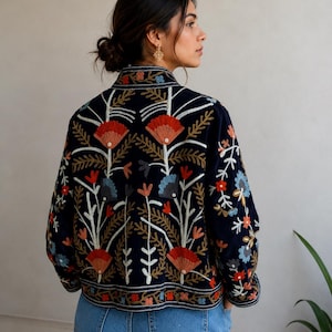 Pu&ograve; includere: Una giacca blu navy scuro con intricati ricami floreali multicolori. Il design presenta grandi fiori rossi e blu con steli e foglie bianche, che coprono la schiena e le maniche. La giacca ha un colletto alto e maniche lunghe.