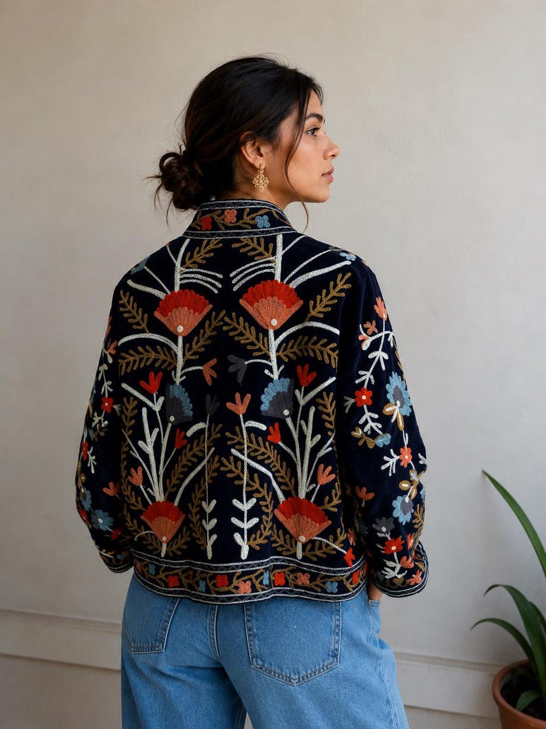 Pu&ograve; includere: Una giacca blu navy scuro con intricati ricami floreali multicolori. Il design presenta grandi fiori rossi e blu con steli e foglie bianche, che coprono la schiena e le maniche. La giacca ha un colletto alto e maniche lunghe.
