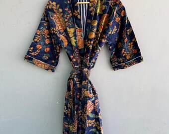 May include: A navy blue floral print robe with orange, yellow, and green accents. The robe has a striped interior and white trim. It is hanging on a wooden hanger against a light gray wall.