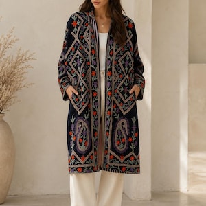 May include: A long, navy blue open-front coat featuring intricate, colourful embroidery in shades of red, purple, and green. The design includes geometric diamond patterns and paisley motifs. The coat has long sleeves and two front pockets.