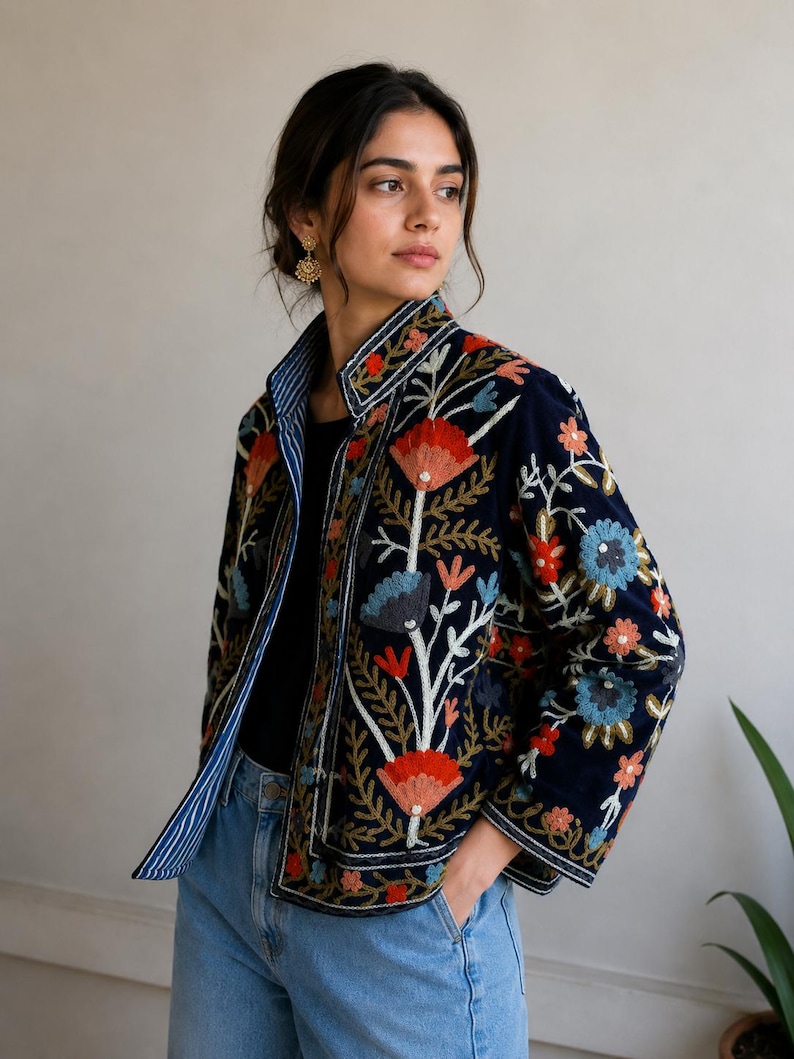 Pu&ograve; includere: Una giacca blu navy con vivaci ricami floreali nei toni del rosso, arancione e azzurro. La giacca presenta un colletto alto, maniche lunghe e una fodera a righe bianche e blu navy visibile lungo l'apertura frontale.