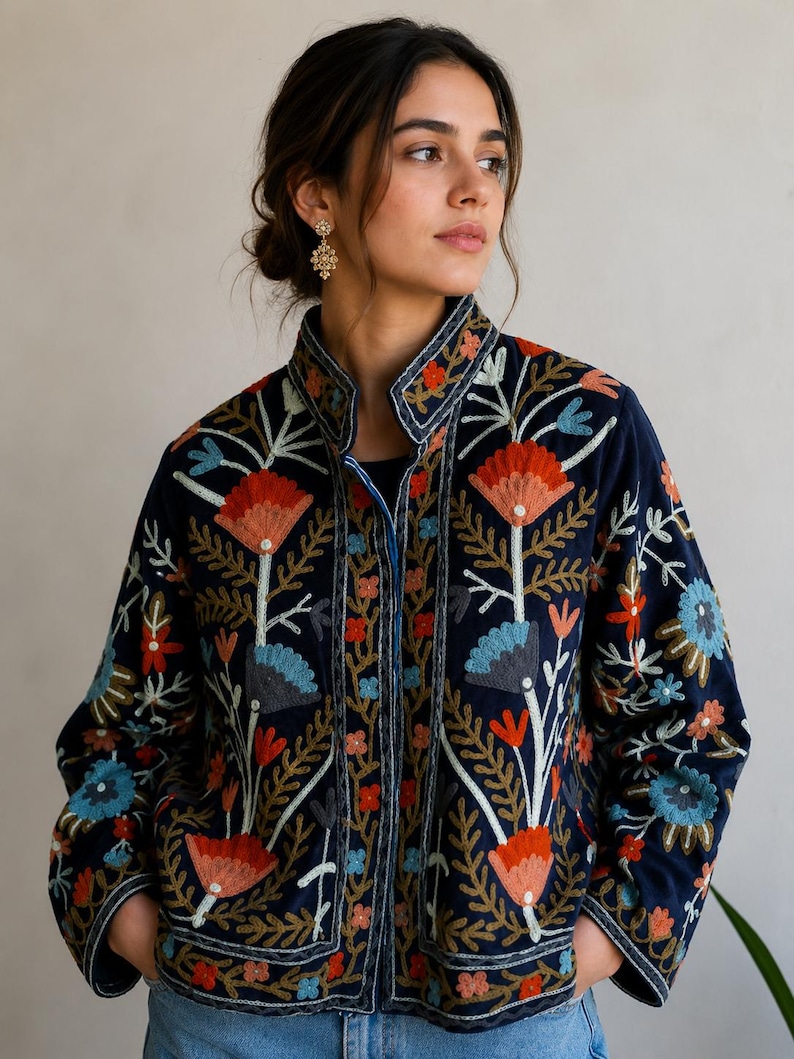 Pu&ograve; includere: Una giacca blu navy scuro caratterizzata da un intricato motivo floreale ricamato multicolore. Il design include grandi fiori arancioni e azzurri con steli e foglie verdi. La giacca presenta un colletto alto e maniche lunghe con ricami.