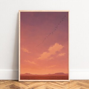 Op de afbeelding: Een ingelijste kunstdruk met een zonsonderganglucht in tinten oranje, roze en paars. Een zwerm vogels vliegt over de lucht. De onderkant van de print toont een landschap van heuvels en bergen.