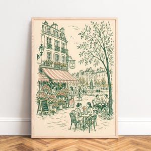 Puede incluir: Una l&aacute;mina enmarcada con un dibujo lineal de una escena callejera parisina con una florister&iacute;a y una cafeter&iacute;a. La ilustraci&oacute;n muestra personas sentadas en mesas, una fuente al fondo y un cartel que dice Fleurs & Caf&eacute; en tinta verde.