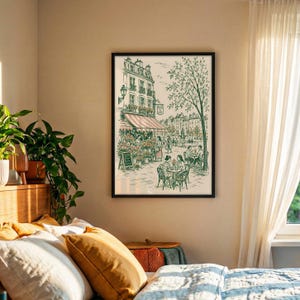 Puede incluir: Una l&aacute;mina de arte enmarcada que presenta un dibujo lineal detallado en verde y crema de una escena callejera parisina con una florister&iacute;a, mesas de caf&eacute; al aire libre y personas. La obra est&aacute; en un marco negro sobre una pared beige.