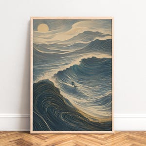 May include: A framed vertical wall art print featuring a stylized illustration of a lone surfer riding a large, swirling ocean wave. The artwork uses a palette of deep blues, creams, and gold accents, with a pale sun visible in the upper sky.