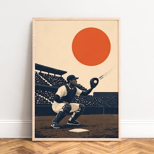 May include: A framed art print depicting a baseball catcher in a crouched position on a field, wearing a white uniform, chest protector, and leg guards. A large orange circle sits in the sky above a dark stadium with rows of spectators.