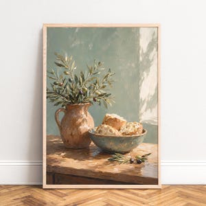 Könnte beinhalten: Ein gerahmter Wandkunstdruck, der ein Stillleben mit einem Terrakotta-Krug voller Olivenzweige neben einer Keramikschale mit Stücken von knusprigem Brot zeigt, die alle auf einer Holzoberfläche mit weichem Licht und Schatten platziert sind.