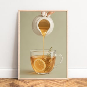 Könnte beinhalten: Ein gerahmter Kunstdruck, der ein weißes Keramik-Kännchen zeigt, aus dem goldener Honig in eine klare Glastasse mit Tee gegossen wird. Der Tee enthält eine leuchtend gelbe Zitronenscheibe und einen grünen Kräuterzweig vor salbeigrünem Hintergrund.