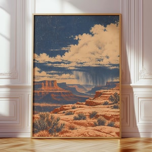 May include: A vertical framed wall art print depicting a desert canyon landscape with red rock formations, sparse desert shrubs, and a dramatic dark blue sky filled with white clouds and a visible rain shower falling over the distant horizon.