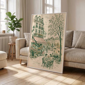 Puede incluir: Una l&aacute;mina de arte enmarcada con un dibujo lineal detallado en verde y crema de una escena callejera parisina. La ilustraci&oacute;n muestra un edificio de varias plantas con un toldo a rayas, una florister&iacute;a, un gran &aacute;rbol y personas sentadas.