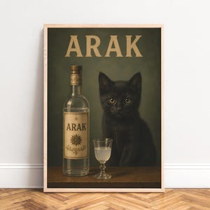 May include: A framed wall art print featuring a black kitten sitting next to a clear glass bottle of Arak and a small stemmed glass containing a cloudy liquid. The word ARAK is printed in large beige capital letters at the top of the poster.
