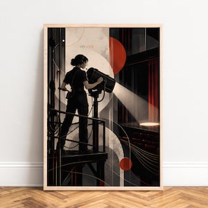 May include: A framed art print featuring a person in dark clothing operating a large stage spotlight from a metal platform. The composition includes geometric circles, red and black accents, and the text ON CUE in a theatre setting.