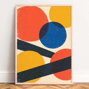 Könnte beinhalten: Ein gerahmter Kunstdruck auf cremefarbenem Hintergrund mit überlappenden geometrischen Formen. Die Komposition besteht aus einem großen roten Kreis, einem gelben Kreis, einem blauen Kreis und zwei dunkelblauen Diagonalbalken.