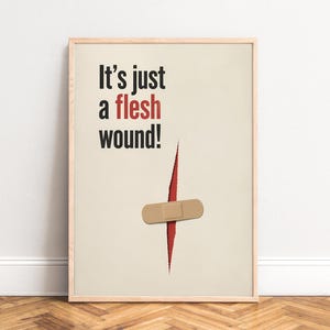 Könnte beinhalten: Gerahmter Druck mit dem Text "It's just a flesh wound!" in Schwarz und Rot. Unter dem Text befindet sich eine rote Schnittgrafik mit einem beigefarbenen Pflaster. Der Hintergrund ist hellbeige.