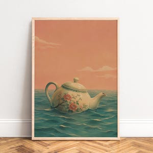 May include: A framed vertical wall art print featuring a ceramic teapot with a floral pattern floating on a calm blue ocean under a soft peach-coloured sky with light clouds. The teapot is white with green trim and pink flower illustrations.