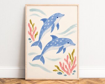 May include: A framed wall art print featuring two blue dolphins with white spots swimming in a light cream background. The illustration includes stylized pink and olive green coral formations and light blue brushstrokes representing water.