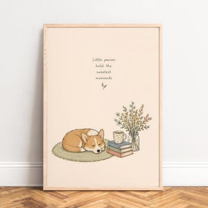 Könnte beinhalten: Ein gerahmter Kunstdruck auf hellbeigem Hintergrund mit einem schlafenden Corgi auf einem runden grünen Teppich, einem Stapel aus drei Büchern, einer Tasse und einer Glasvase mit Wildblumen. Der Text lautet: Little pauses hold the sweetest moments.